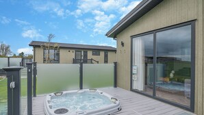 A hot tub on a wooden deck with a sliding glass door to a room.