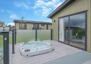Un jacuzzi en una terraza de madera con una puerta corrediza de vidrio hacia una habitación.