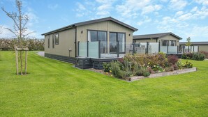 A modern mobile home with a large glass window, a deck, and a well-maintained garden.