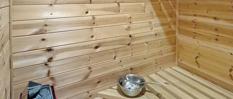 A sauna room with wooden walls and a metal basin.