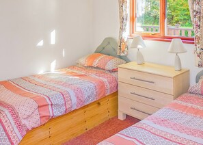 Een slaapkamer met een enkel bed, een nachtkastje met lampen, een dressoir en een raam met gordijnen.