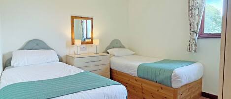 A bedroom with two beds, a bedside table with lamps, a mirror, and a window with curtains.