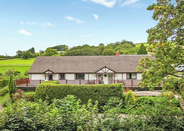 Een tweelaags huis met een veranda, omgeven door weelderige begroeiing en een heldere lucht.