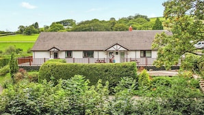 A two-story house with a porch, surrounded by lush greenery and a clear sky. - Cottage with one double and two twin. (St Clears)