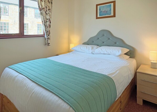 A neatly made bed with a quilted green blanket, a headboard, and a bedside table with a lamp.