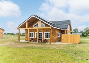 Une cabane en rondins avec une véranda, des tables de pique-nique et une cour clôturée.