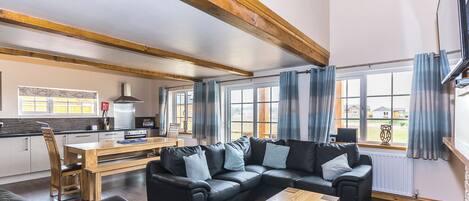 Ein modernes Wohnzimmer mit einem Ecksofa, einem Couchtisch aus Holz und einer Küche im Hintergrund.