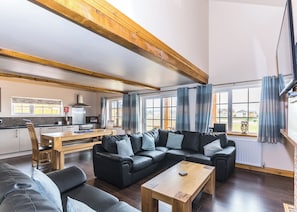 Ein modernes Wohnzimmer mit einem Ecksofa, einem Couchtisch aus Holz und einer Küche im Hintergrund.