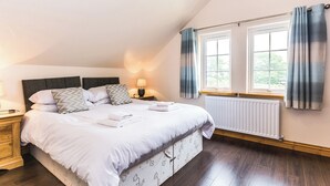 Un dormitorio con una cama grande, una mesita de noche, una lámpara, una ventana con cortinas y un radiador.
