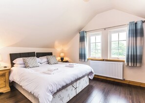 A bedroom with a large bed, a nightstand, a lamp, a window with curtains, and a radiator.