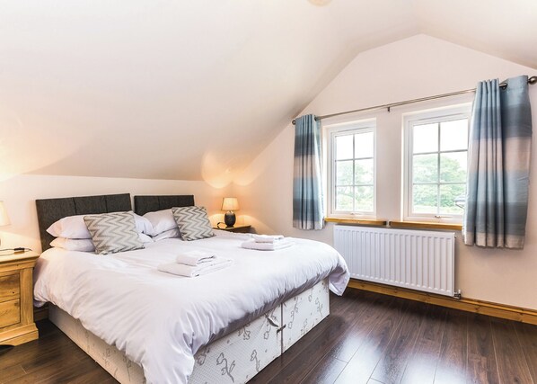 A bedroom with a large bed, a nightstand, a lamp, a window with curtains, and a radiator.