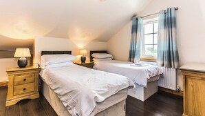 Un dormitorio con dos camas, una mesita de noche con lámpara, una ventana con cortinas y suelo de madera.