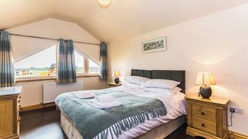 A bedroom with a bed, bedside tables, a lamp, a window with curtains, a radiator, and a painting on the wall.