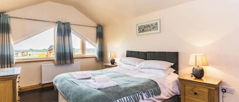 A bedroom with a bed, bedside tables, a lamp, a window with curtains, a radiator, and a painting on the wall.
