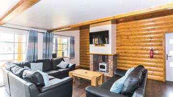 L’intérieur d’une cabane en rondins, avec une cheminée, deux canapés en cuir noir, une table basse en bois et une grande fenêtre avec des rideaux.