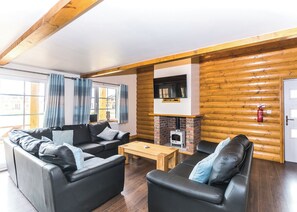 L’intérieur d’une cabane en rondins, avec une cheminée, deux canapés en cuir noir, une table basse en bois et une grande fenêtre avec des rideaux.