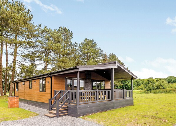 Une cabane moderne avec une façade en bois, une véranda et une allée en gravier.