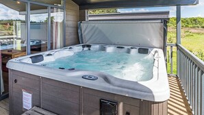 Un jacuzzi en una terraza de madera con cerramiento de vidrio, un banco y vistas al exterior.