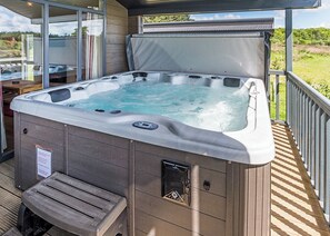 Un bain à remous sur une terrasse en bois, doté d’une paroi vitrée, d’un banc et offrant une vue sur l’extérieur.