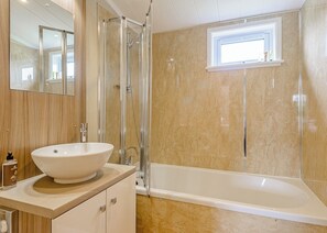 Une salle de bain dotée d’une grande baignoire, d’une douche à parois de verre, d’un lavabo avec un plan de travail en marbre et d’un miroir au-dessus du lavabo.