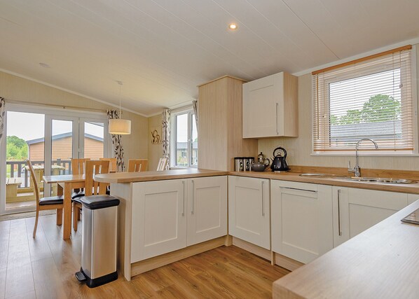 A modern kitchen with white cabinets, a wooden countertop, and a window with blinds.