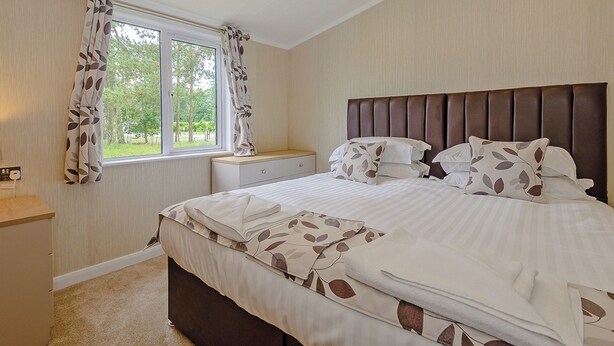 Un dormitorio con cama, una mesita de noche, una ventana con cortinas y vistas al verdor exterior.