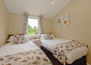 A bedroom with two beds, a window with curtains, a bedside table with a lamp, and a wall painting.