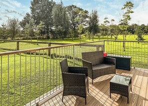 Eine Terrasse im Freien mit Korbmöbeln und einem Glastisch, umgeben von einem Metallzaun und einer Rasenfläche.