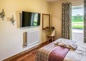 Quarto com cama, escrivaninha, televisão, radiador e vista para um jardim.