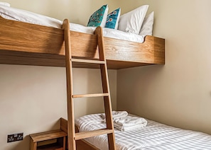 Una cama litera con una escalera de madera, almohadas blancas y una manta a cuadros.