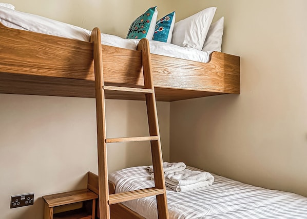 A bunk bed with a wooden ladder, white pillows, and a checkered blanket.