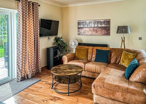 A living room with a leather sofa, a round coffee table, a flat-screen TV, a painting, a lamp, and a fan.