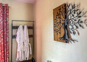 Ein Zimmer mit einer Holzwandkunst eines Baumes, einem Metallregal mit Handtüchern und roten Vorhängen mit einem floralen Muster.