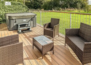 A deck with wicker furniture, a hot tub, and a wooden floor.