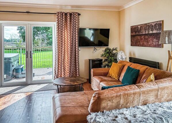 Una sala de estar con un sofá de cuero, un televisor de pantalla plana, una mesita y un ventanal corredero que da a un jardín.