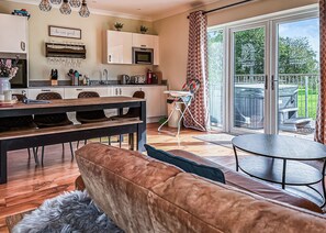 Uma cozinha moderna com armários brancos, um espaço de refeições com mesa de madeira e sofá marrom, e uma porta de vidro deslizante para um pátio externo.