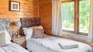 A wooden cabin bedroom with a bed, bedside table, lamp, and window with curtains.