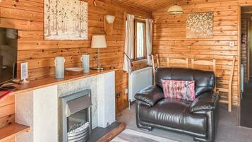 A cozy cabin interior with a fireplace, leather sofa, wooden walls, and a dining area.