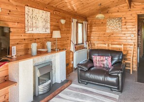 A cozy cabin interior with a fireplace, leather sofa, wooden walls, and a dining area.
