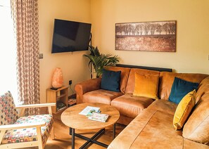 Una sala de estar con un sofá, una mesa de centro, un televisor, un cuadro y una planta.