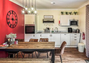 Una cocina moderna con armarios blancos, horno empotrado, microondas y un comedor con mesa y sillas de madera.