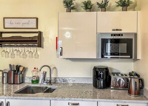 Una cocina equipada con microondas, cafetera, tostadora y lavamanos.