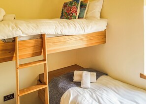 Una cama litera con escalera de madera, una cama individual abajo y un cojín colorido.