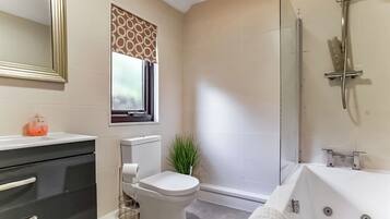 A bathroom with a toilet, bidet, bathtub, and a window with patterned curtains.