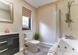 Une salle de bain équipée de toilettes, d’un bidet, d’une baignoire et d’une fenêtre agrémentée de rideaux à motifs.