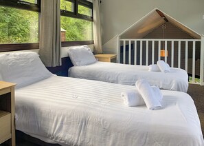 Une chambre d’hôtel avec deux lits, une tête de lit en bois, une fenêtre avec des rideaux et un petit balcon donnant sur un espace verdoyant.