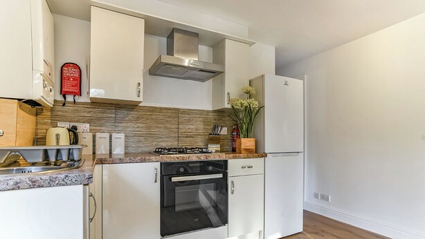 A modern kitchen with white cabinetry, a gas stove, an oven, and a stainless steel range hood. - Woodpecker Lakeside Lodge (Caerwys, Flintshire)