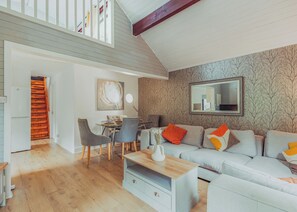 A modern living room with a dining area, wooden staircase, and a loft space.