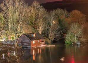 Une cabane en bois au bord d’un lac paisible, au milieu des arbres, la nuit.