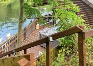 Une terrasse en bois avec un jacuzzi, entourée d’eau et de verdure.
